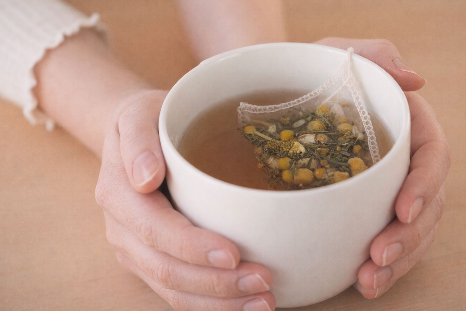 Händer som håller en varm kopp örtte med en tepåse fylld av kamomill.